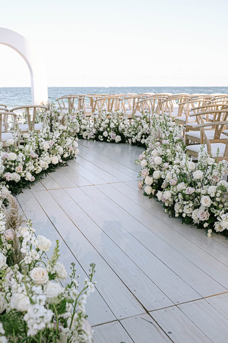 Seaside wedding ceremony with floral arch and ocean backdrop, arranged by Table 6 Productions. Perfe.