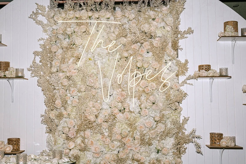 Elegant wedding floral backdrop with neon "The Vow" sign for special occasions.