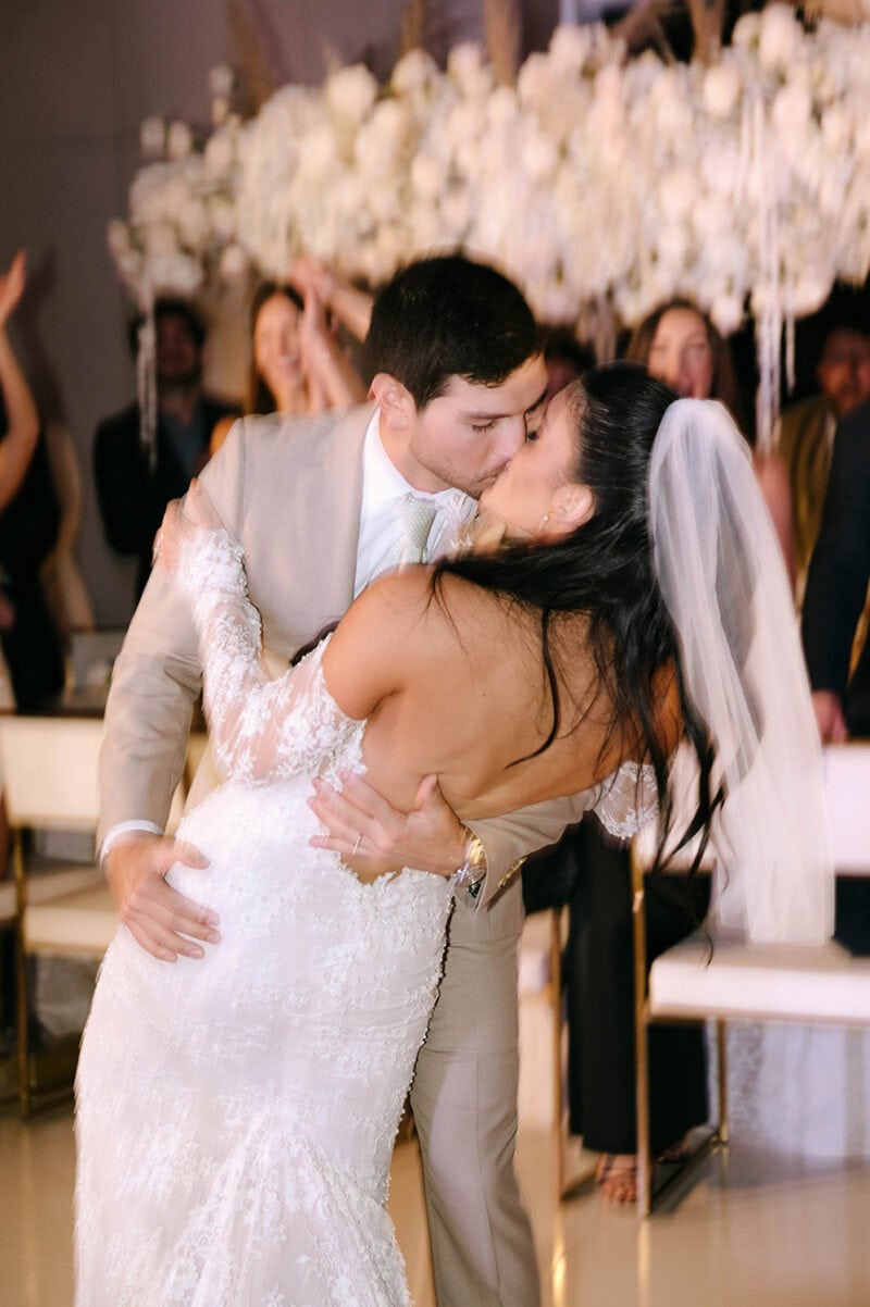Wedding couple kissing during ceremony with guests in background.
