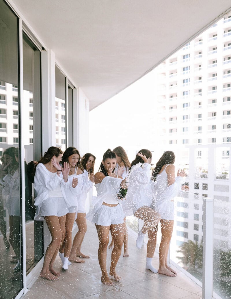Group of women enjoying a water splash on a balcony in white outfits.