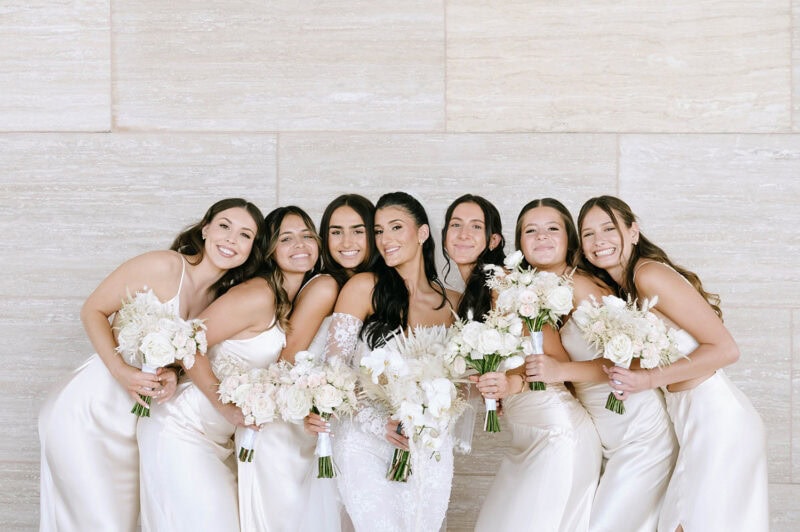 Bridesmaids in white dresses holding bouquets, smiling at a wedding event.