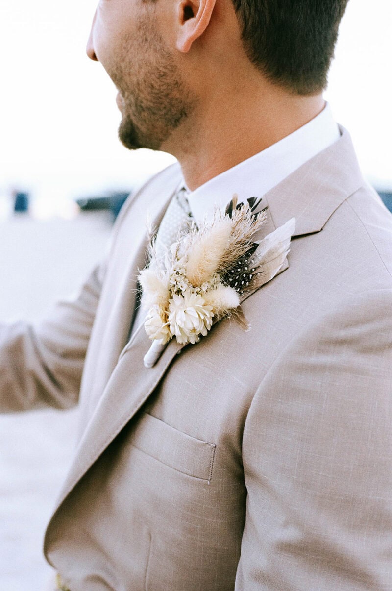 Elegant wedding boutonniere with feathers and white flowers on groom's beige suit.