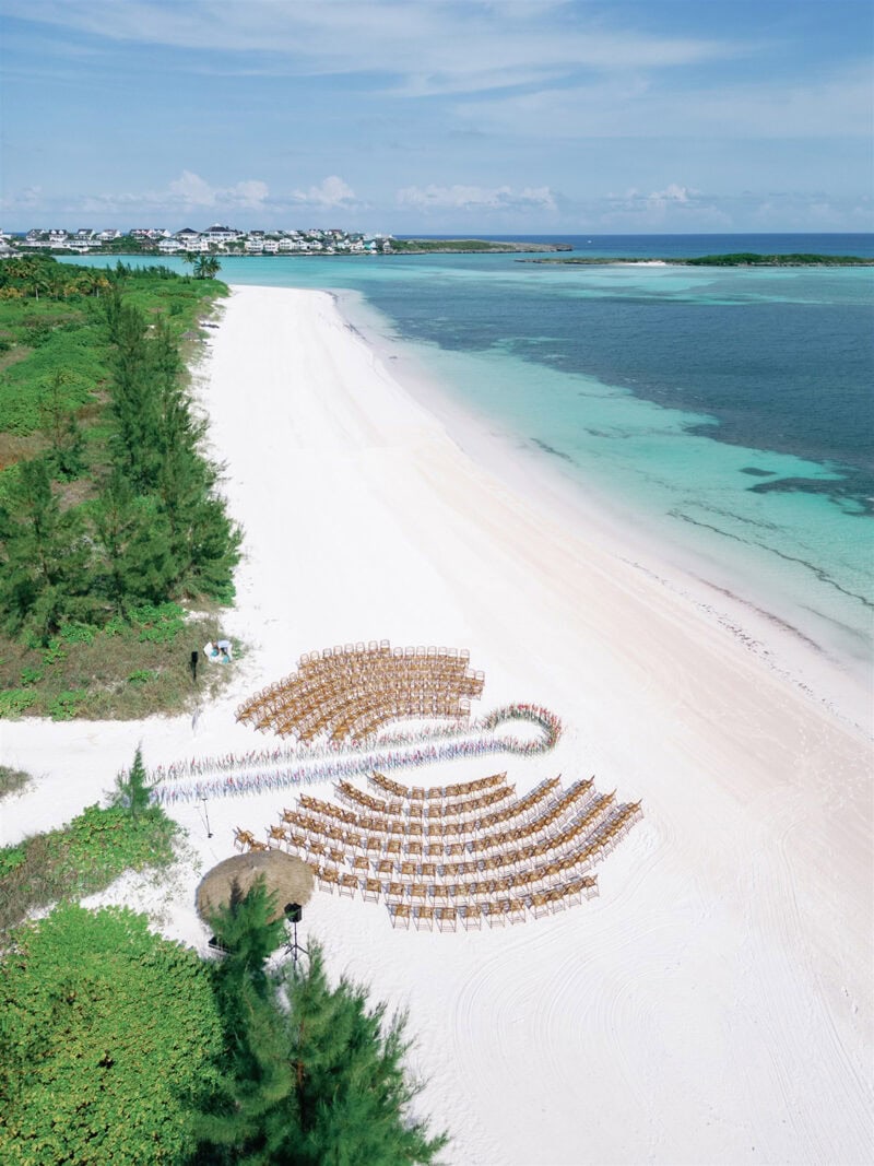 Beach wedding setup with chairs and umbrellas on white sand.