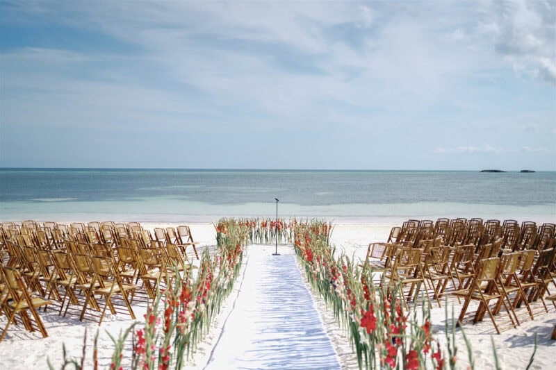 Beachside wedding ceremony setup with chairs and floral aisle.
