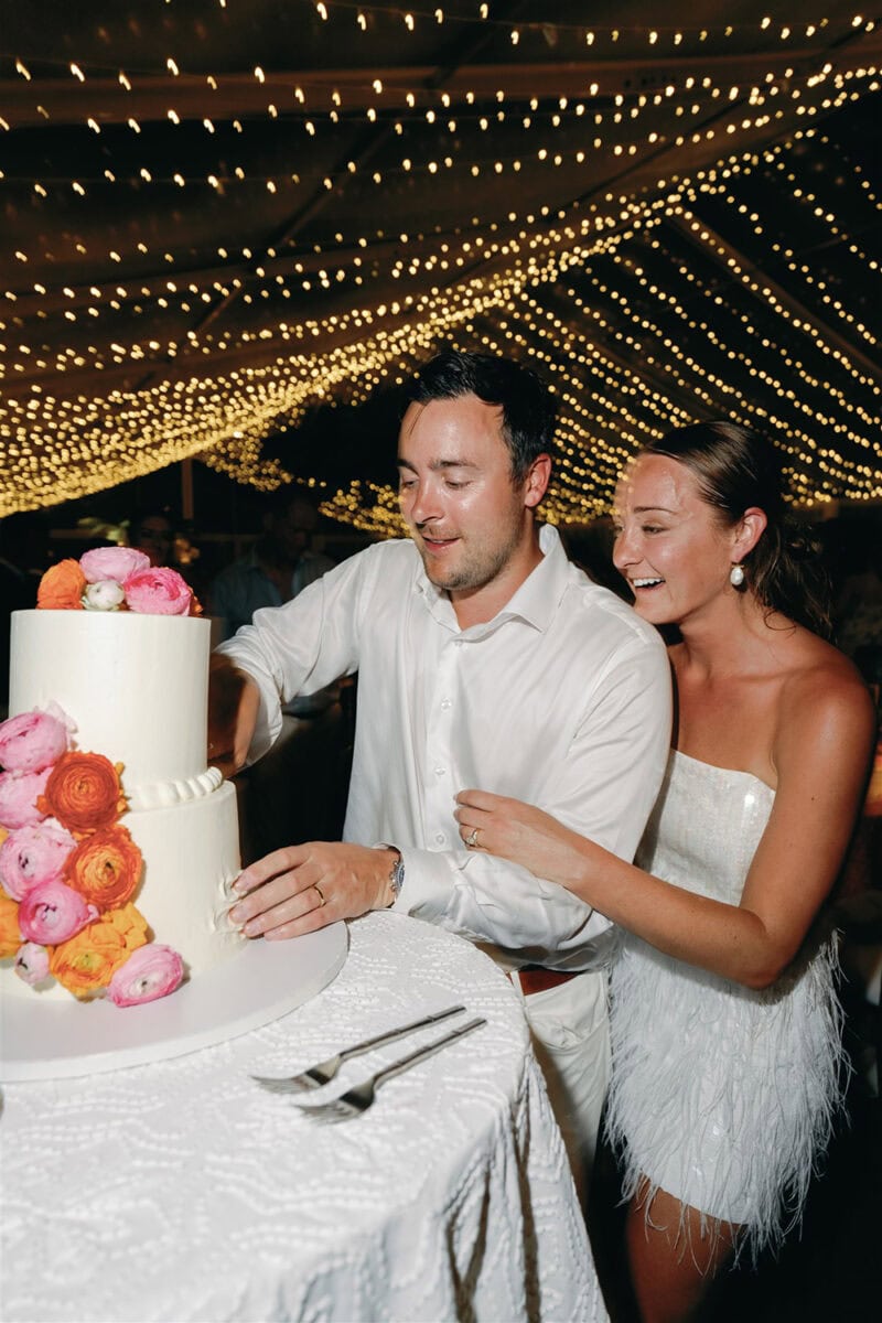 Bride and groom cutting a wedding cake decorated with pink and orange flowers at their celebration.