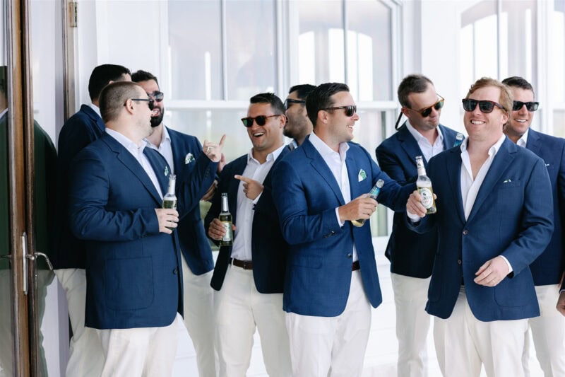 Groomsmen in blue suits enjoying drinks and laughter at the wedding reception.