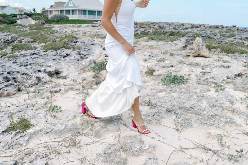 Bride walking on rocky beach in a white wedding dress and pink heels.