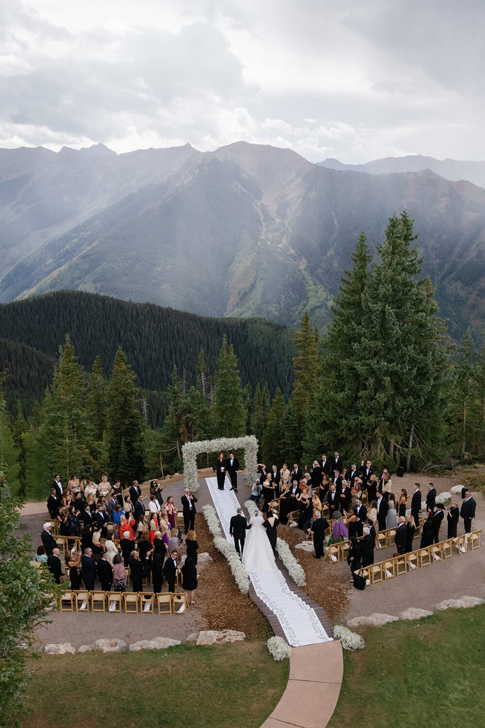 Scenic outdoor wedding ceremony set in Colorado mountains with guests and couple under floral arch.