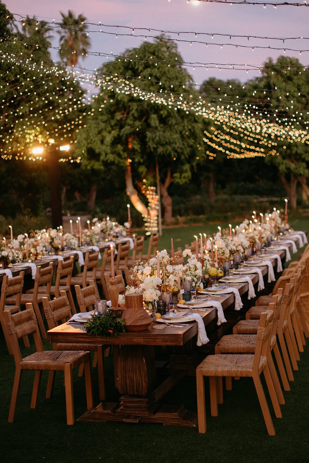 Outdoor wedding reception with long decorated tables and string lights.