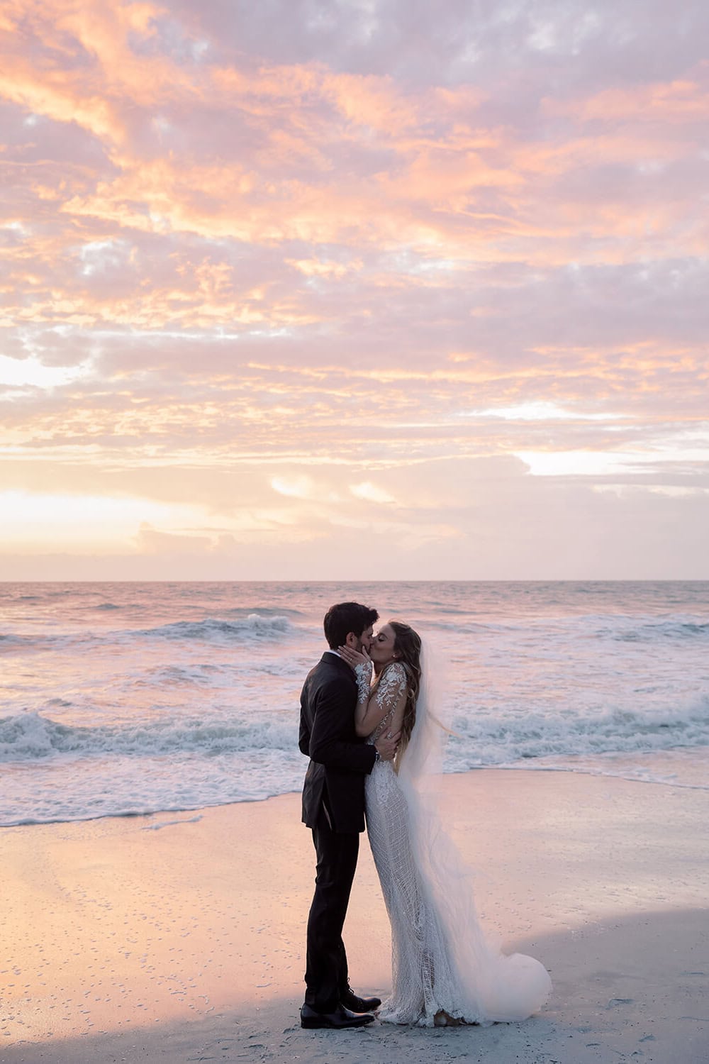 Beach wedding couple at sunset with ocean waves in the background.