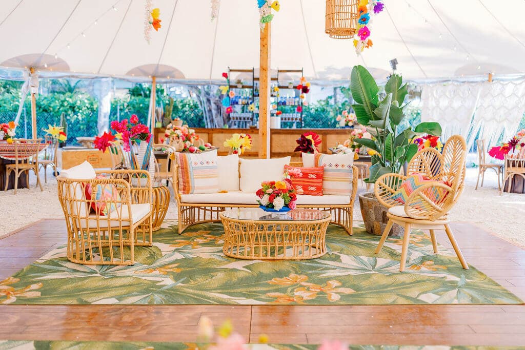 Elegant tropical-themed wedding lounge with rattan furniture and vibrant floral decor.