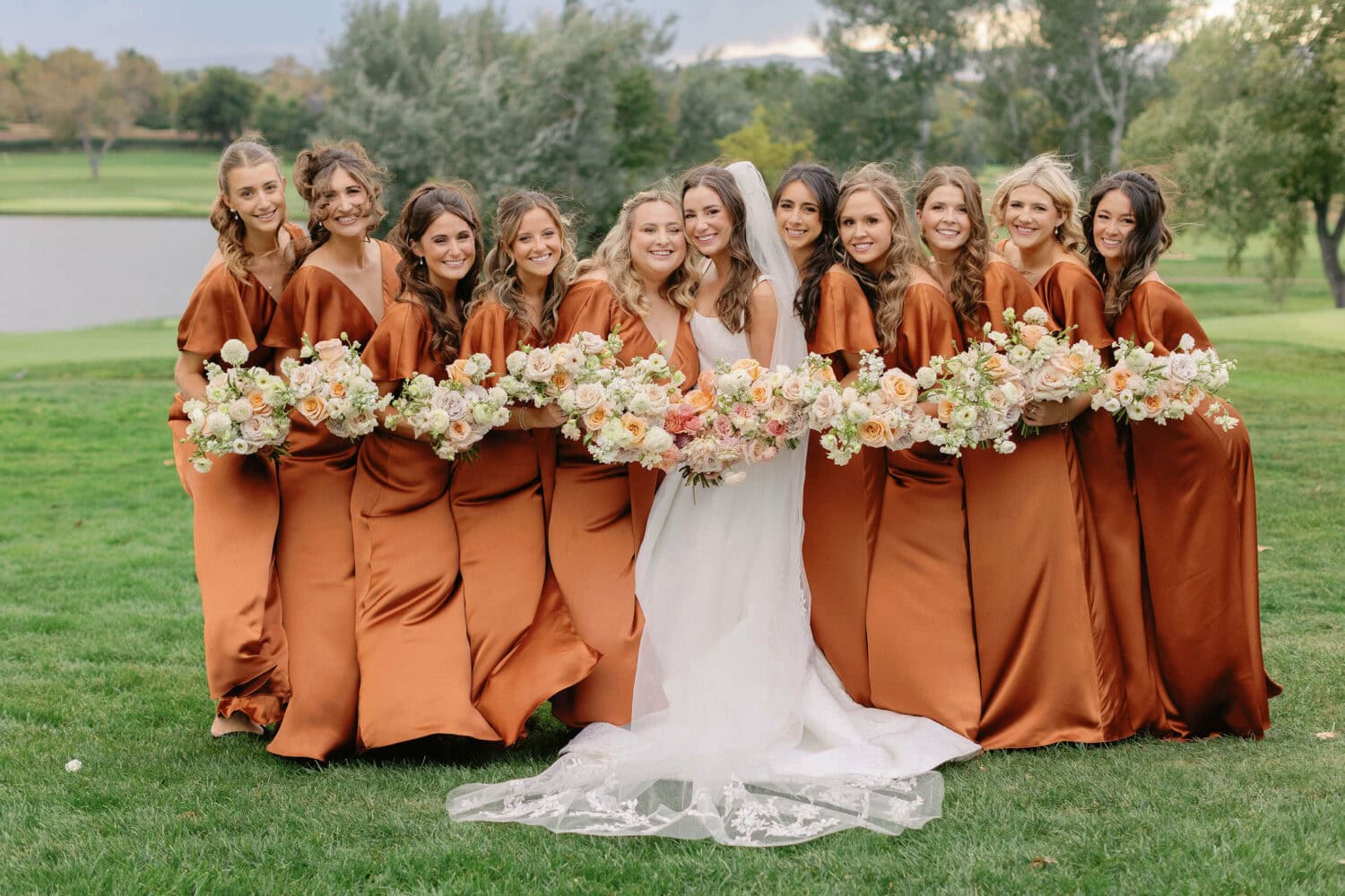 Wedding party with bride and bridesmaids outdoors on a lush green lawn.