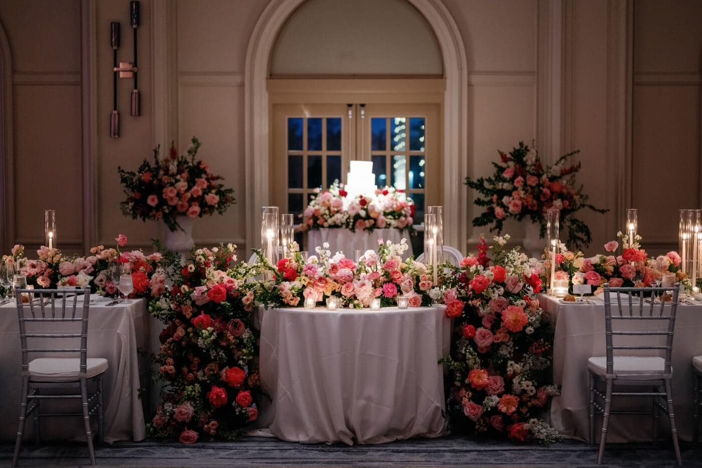 Beautifully decorated wedding table with pink and white flowers, candles, and elegant chairs.