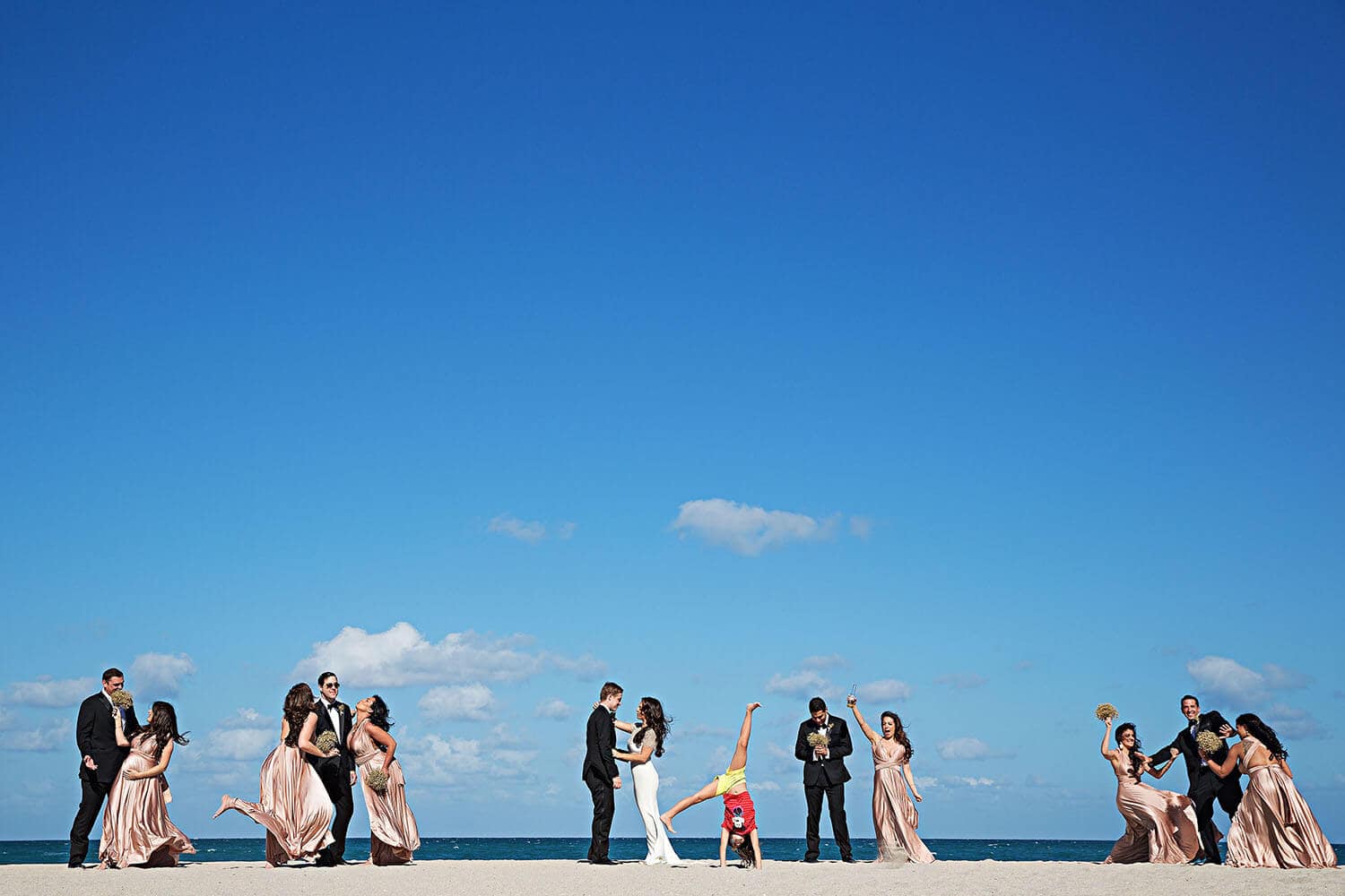 Beach wedding procession with couples and a child performing a handstand.