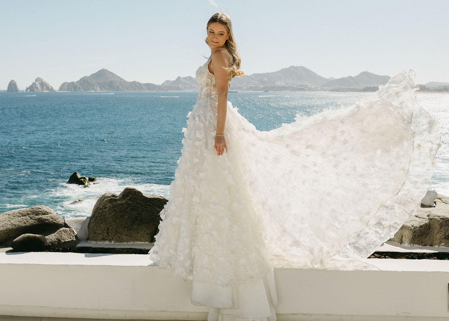 Bride in a flowing wedding gown with ocean backdrop.