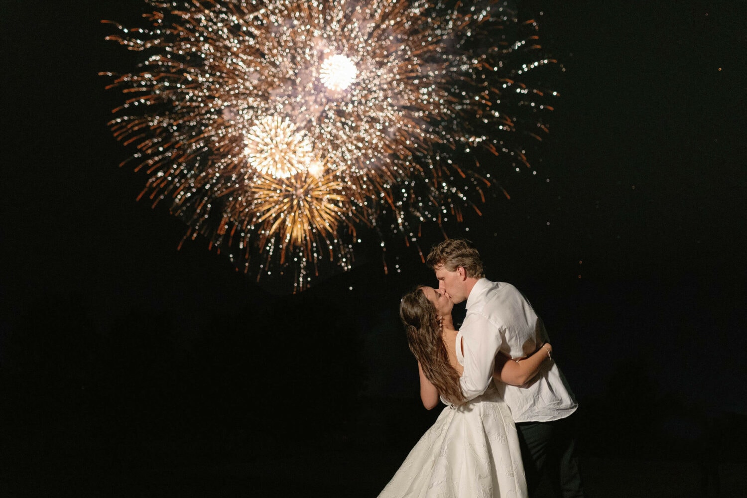 Bride and groom sharing a kiss during fireworks display.