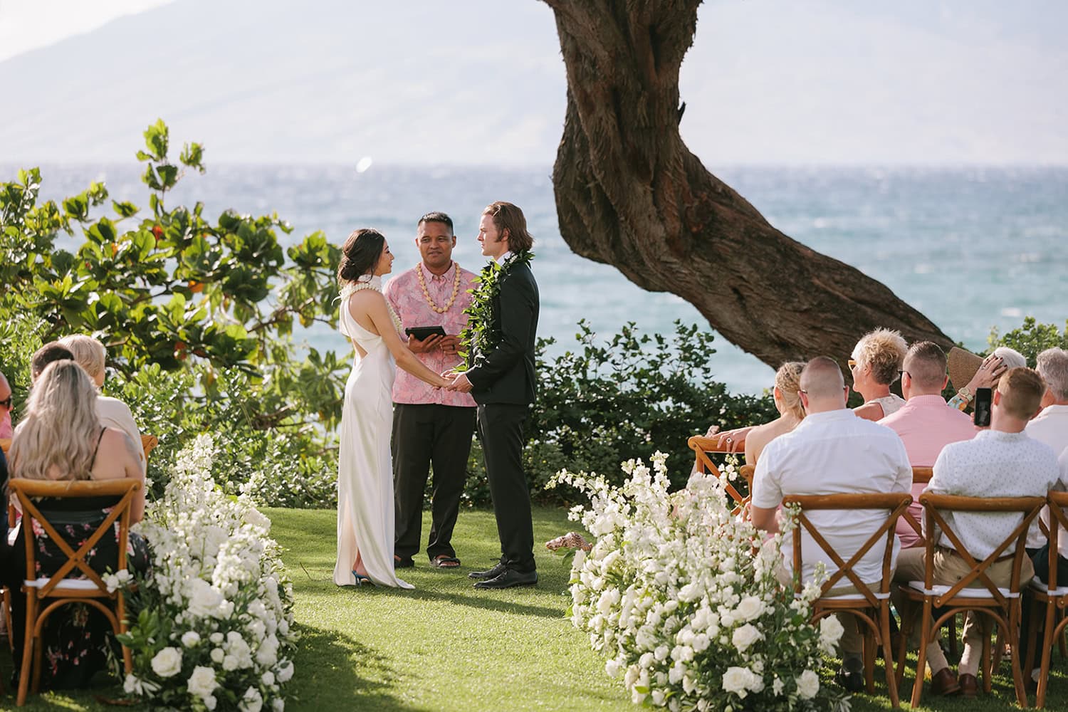 Beautiful destination wedding ceremony outdoors with ocean view and lush greenery.