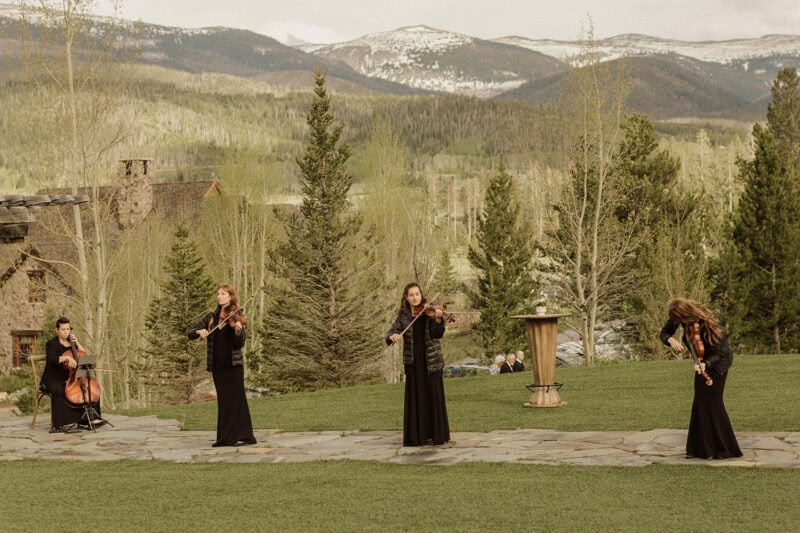 Elegant string musicians playing classical music in a scenic mountain setting.