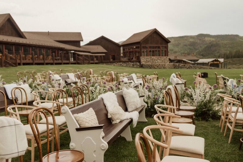 Beautiful outdoor wedding ceremony area with vintage chairs, floral decor, and scenic mountain backd.