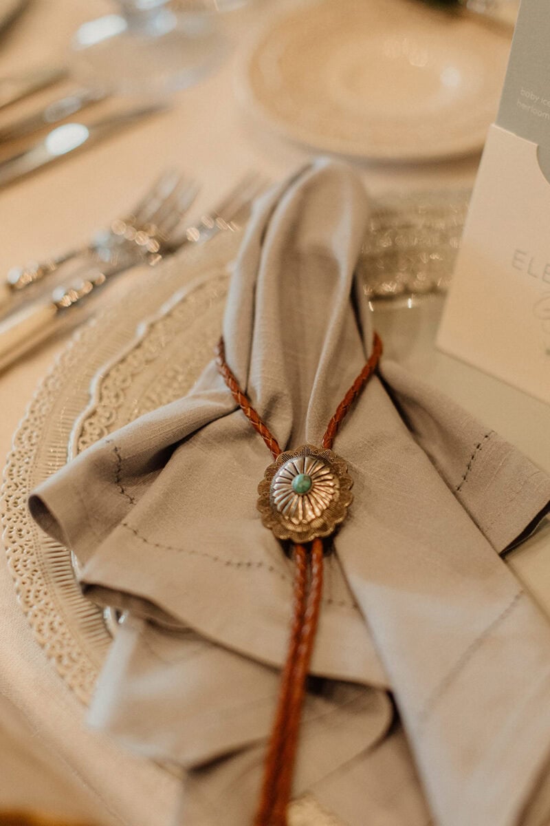 Elegant wedding table setting with a napkin tied with a decorative brooch and rustic twine.