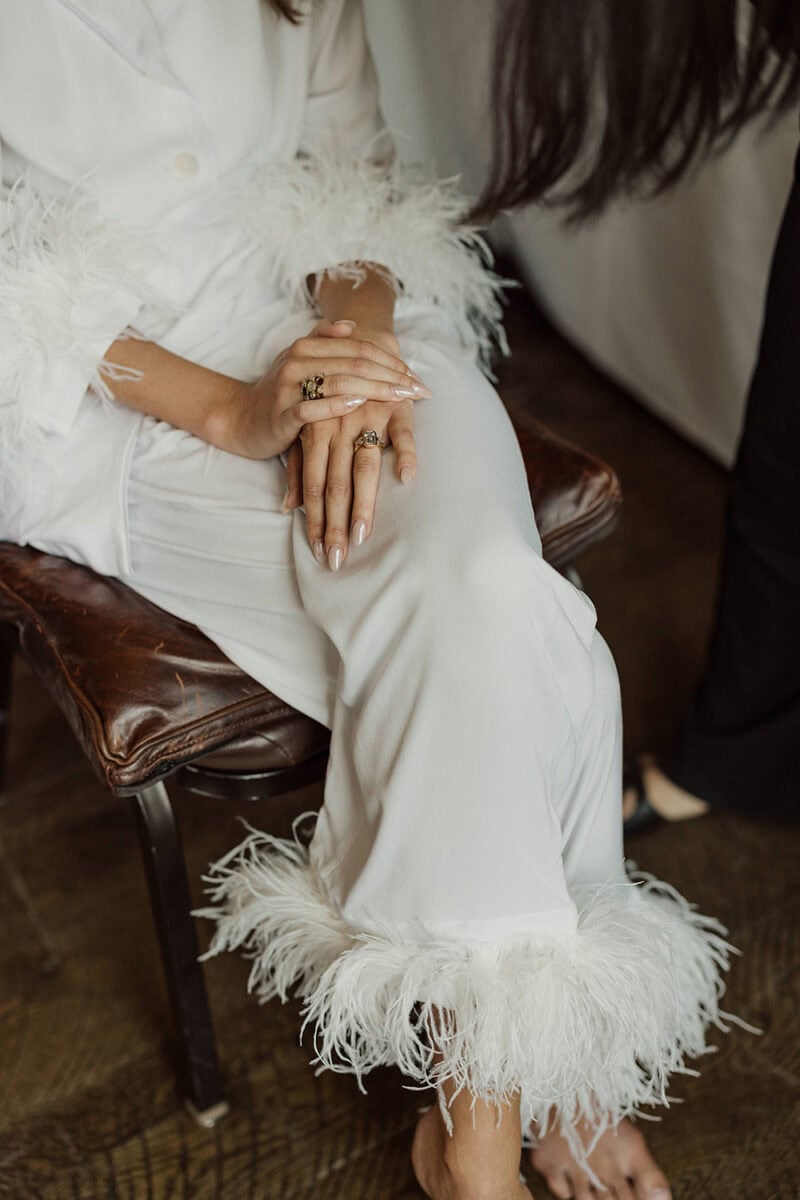 Close-up of bride's hands with wedding rings, sitting on a chair during wedding celebration.