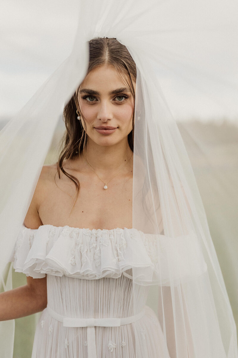 Bride in wedding dress with veil, looking at camera during outdoor wedding.